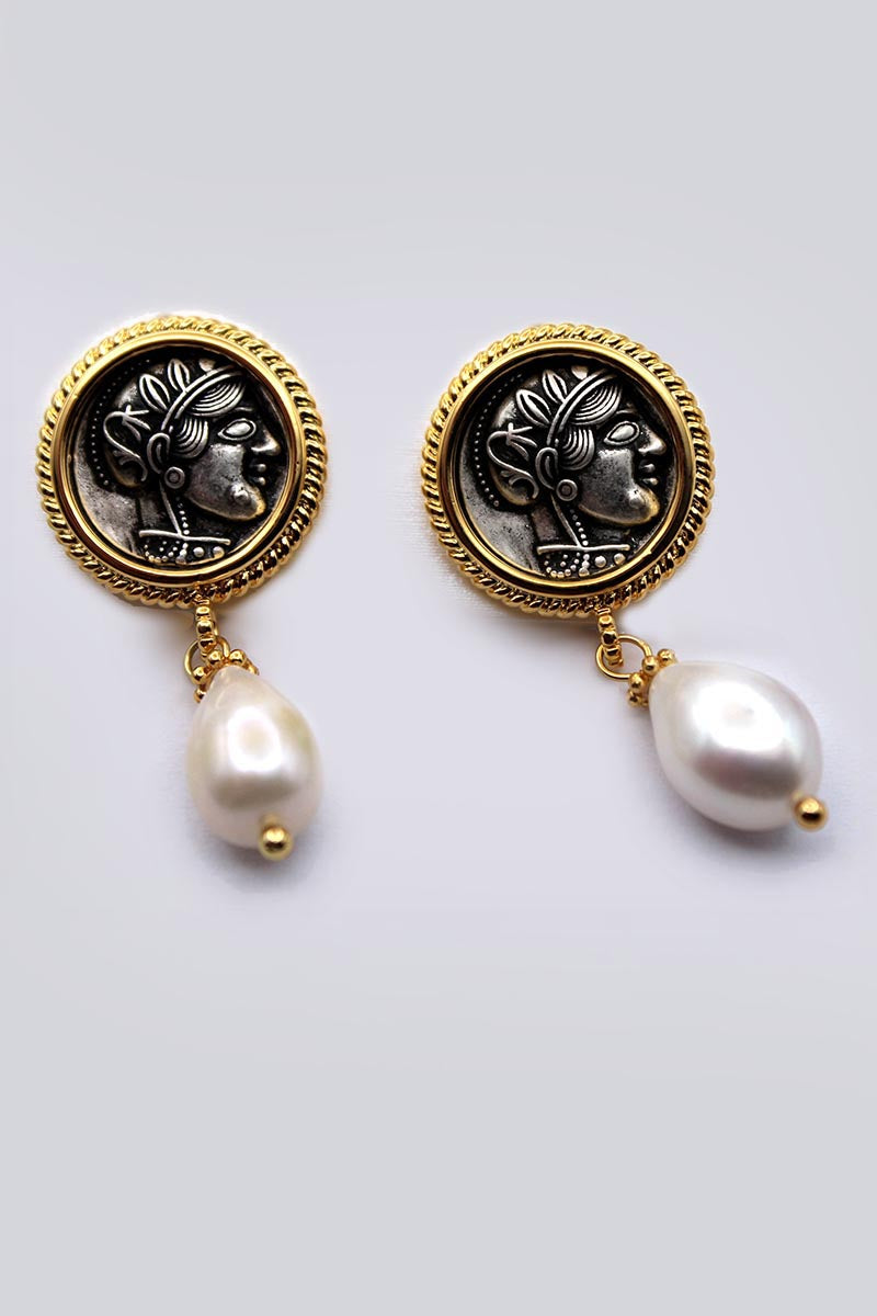Pair of earrings with gold and black circular designs and white pearls on a light gray background