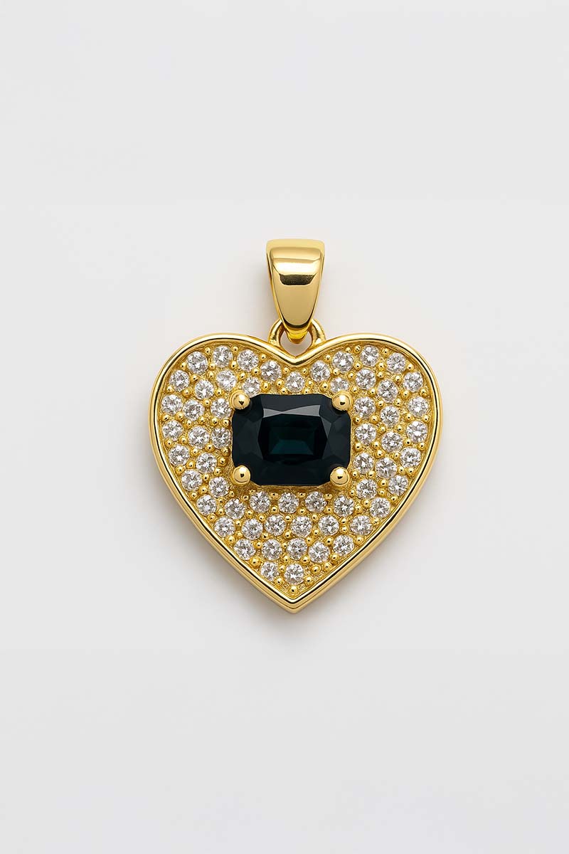 A gold-colored pendant with a heart shape, featuring a central black gemstone surrounded by smaller clear stones set in a pavé pattern.