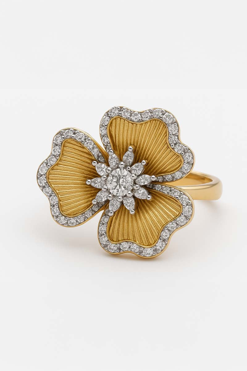 A gold floral ring with grooved petals and a sparkling center stone, surrounded by cut stones