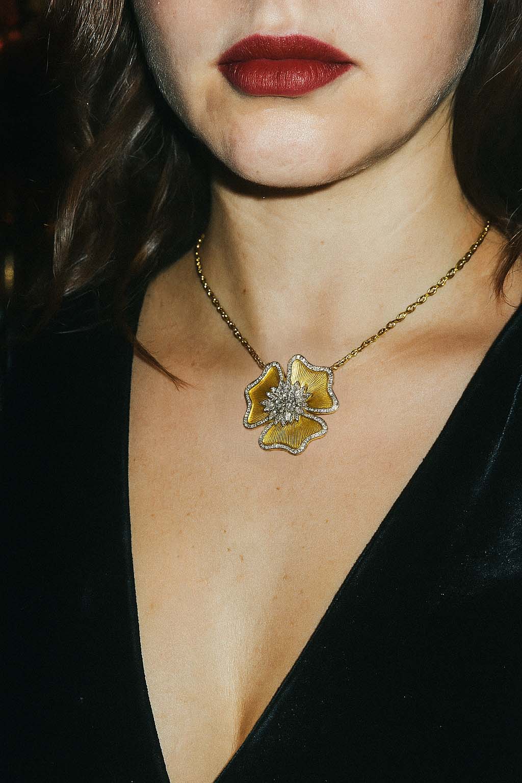 Close-up of a necklace with a yellow flower pendant worn by a person.