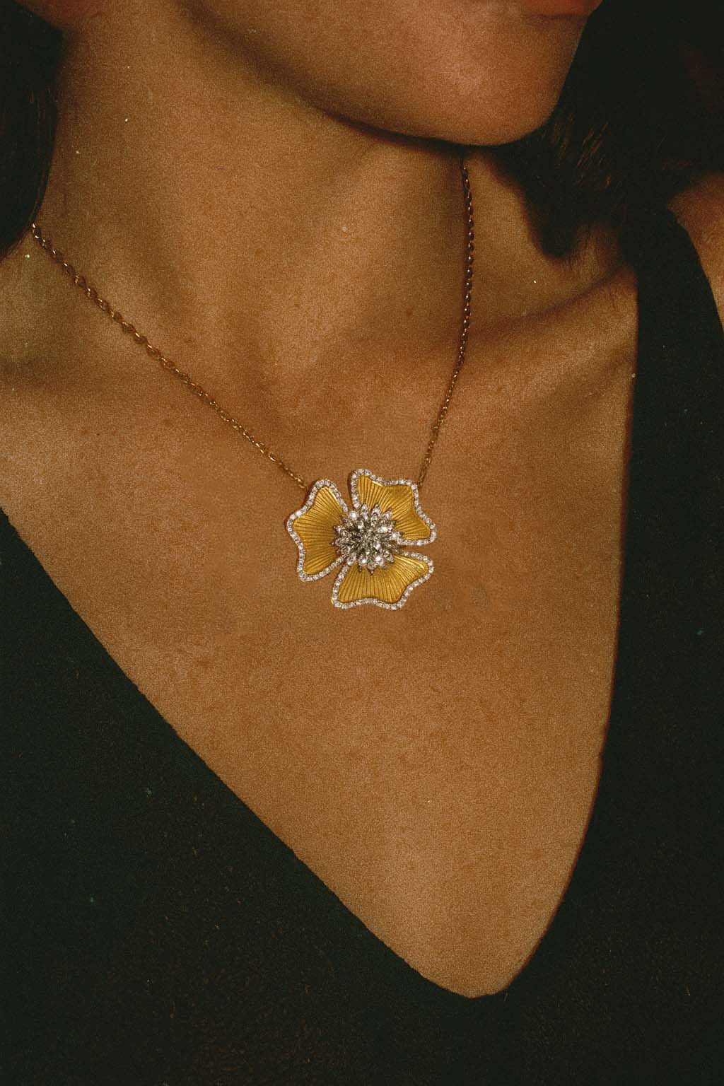 Necklace with a yellow flower pendant on a person's neck against a dark background