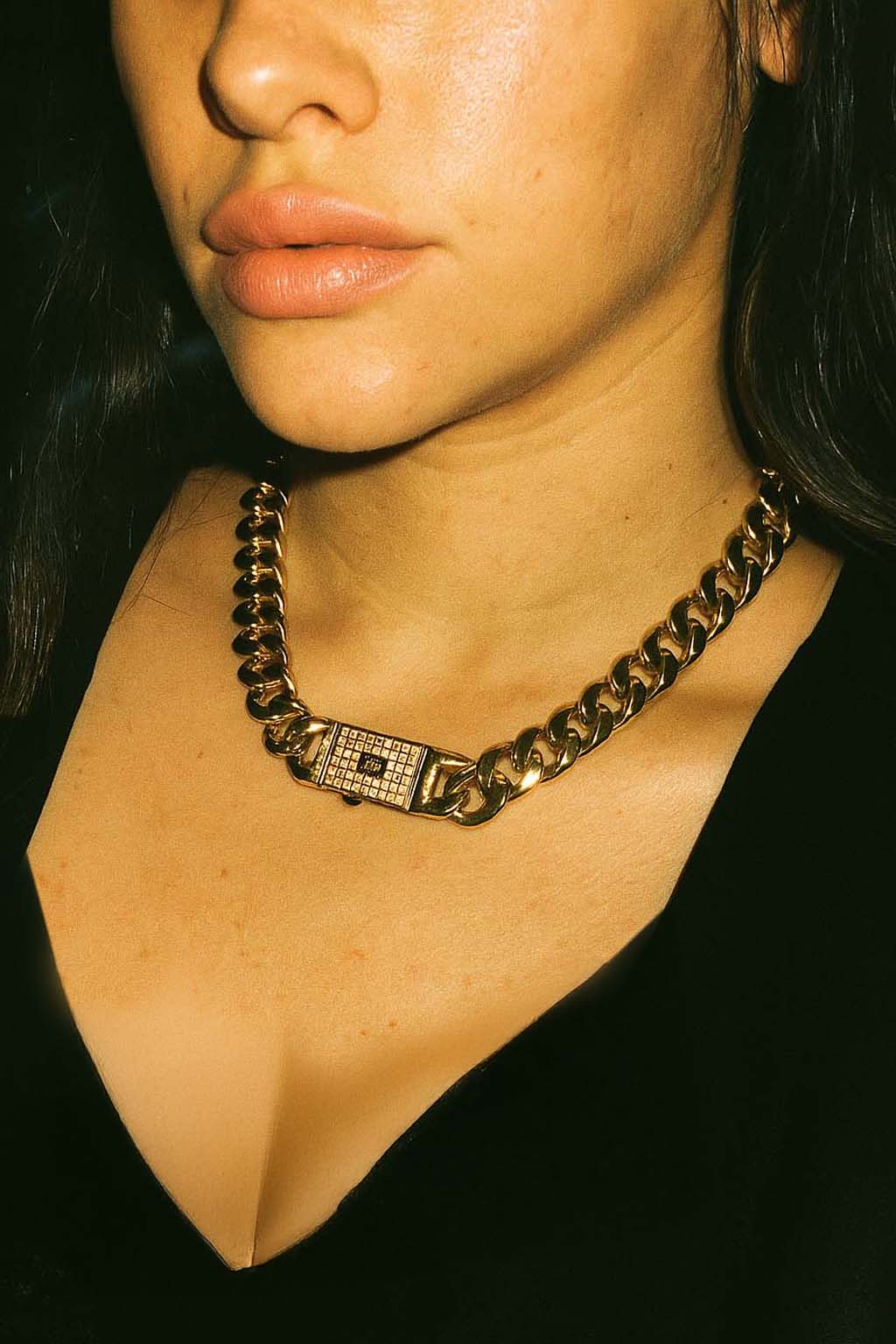 Close-up of a person wearing a gold chain necklace with a black background